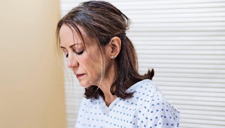 A woman in a medical gown sits in a doctor's office looking down.