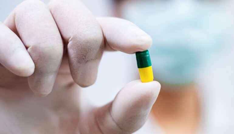 gloved hand holds yellow and green capsule