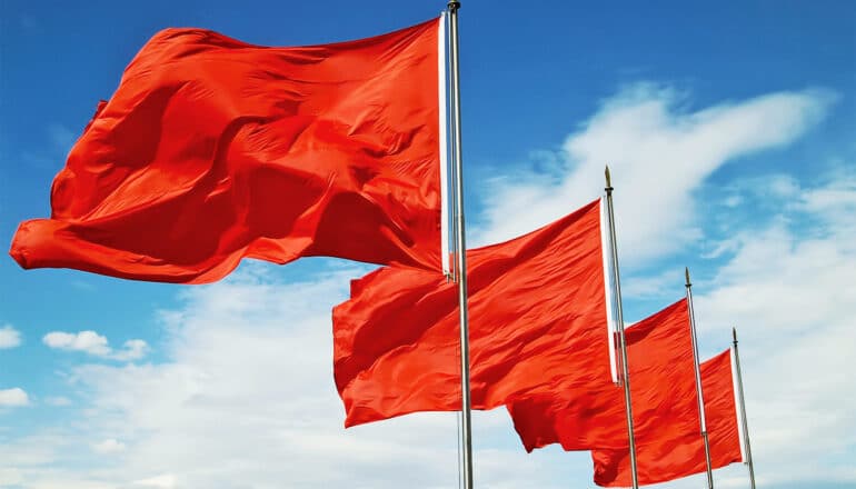 A row of 4 red flags against a blue sky.