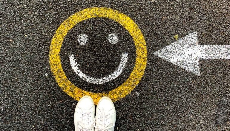 white sneakers on pavement with smiley face and arrow toward it