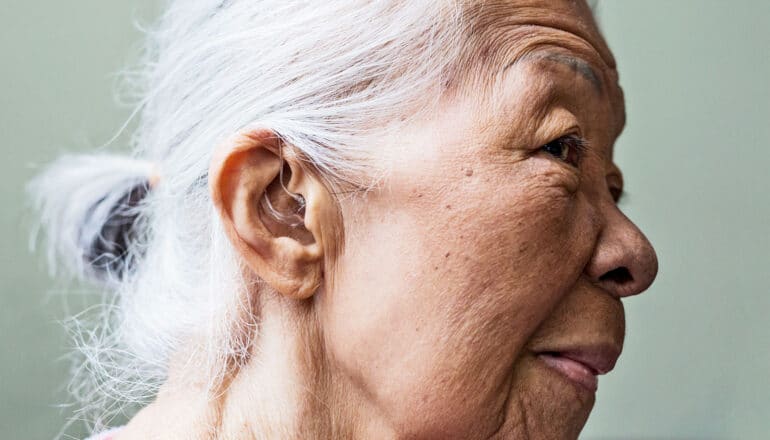 A woman looks off camera while wearing a hearing aid in her ear.