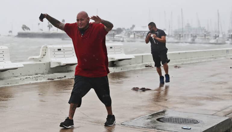 Two men walk through intense wind ahead of a hurricane.