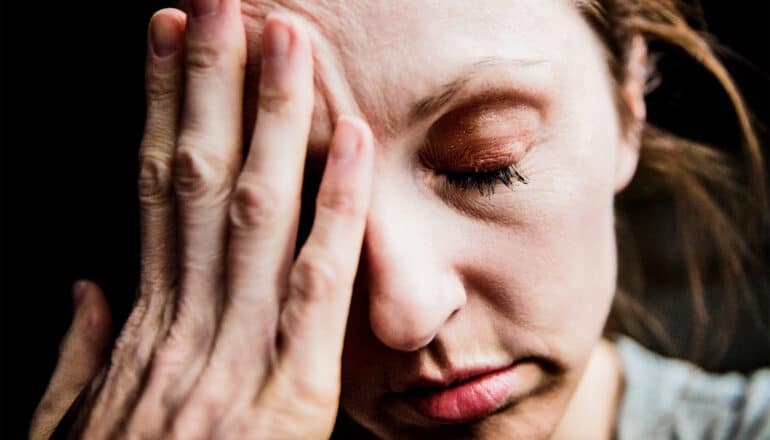 A woman puts her hand on her forehead and closes her eyes.