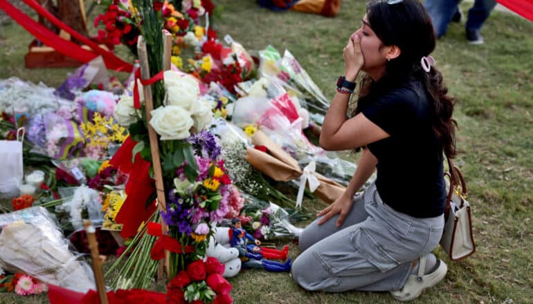 person kneels, crying, in front of memorial