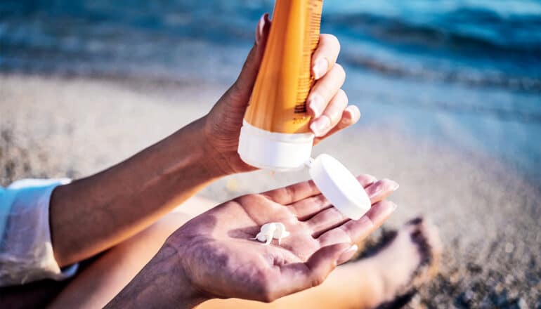 A person squeezes a bottle of sunscreen into their palm while they're at the beach.