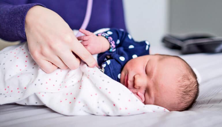 A midwife swaddles a newborn baby on a table.