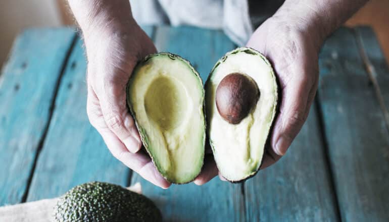 hands hold avocado halves over teal wooden table