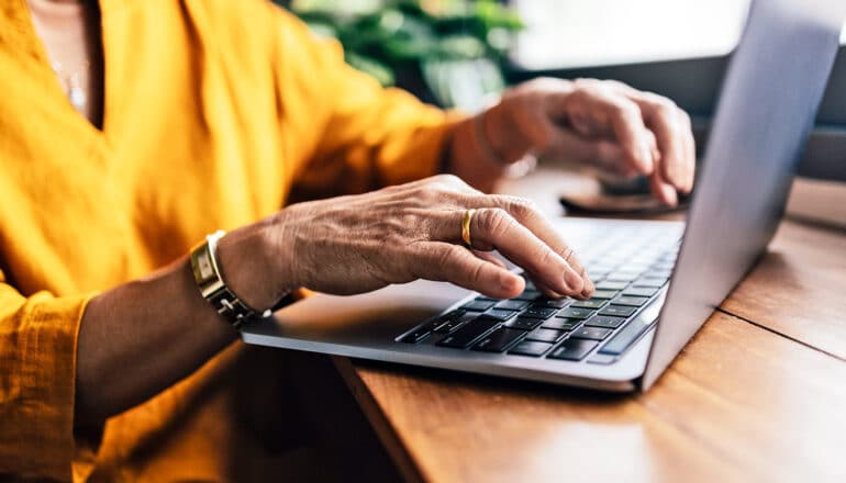 A woman in a yellow top uses a laptop on a table.