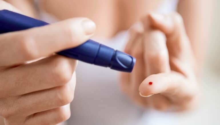 A person uses a finger-prick device to draw a drop of blood from their finger.