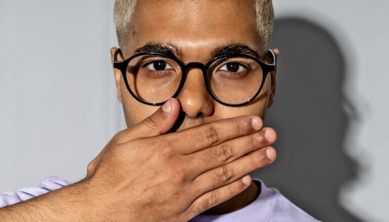 person in glasses covers mouth with hand