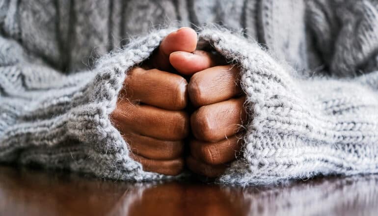 A person clasps their hands together anxiously while resting them on a table.