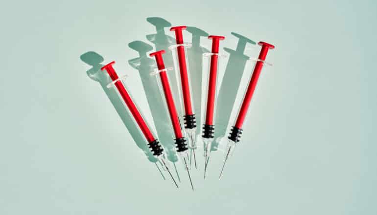 5 red syringes on pale green surface