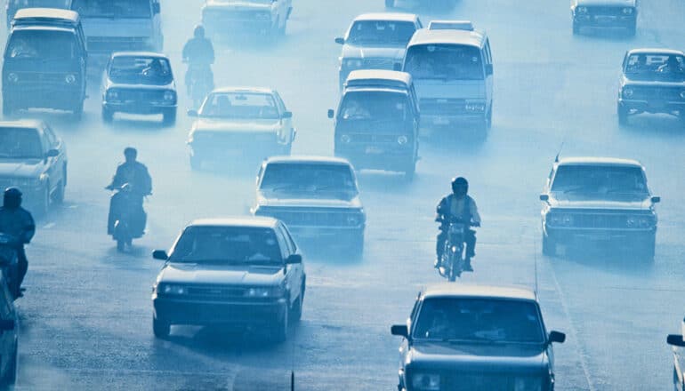 Cars and motorcycles on a multi-lane high way drive through heavy smog.