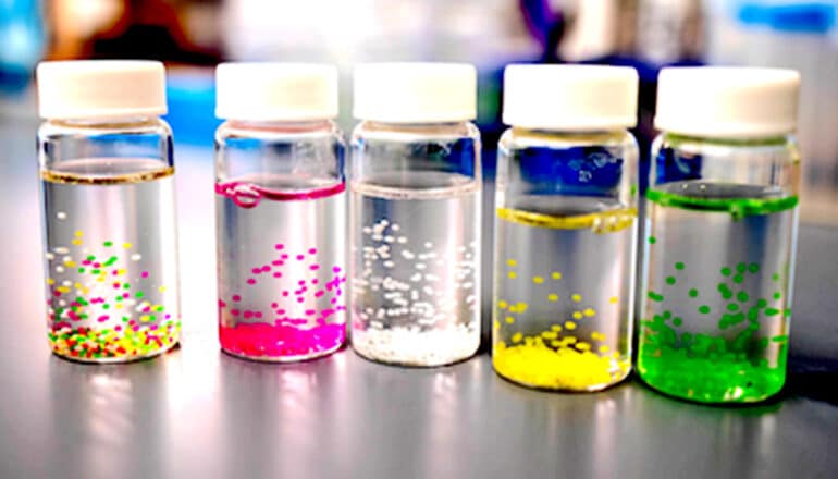 Several glass vials with white cats have different colored biomaterial specks floating in them.