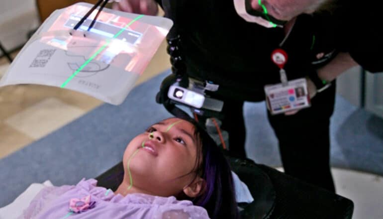 A young patient getting radiation treatment watches a video while laying down.