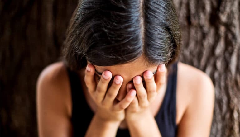 A young woman cries with her hands over her face.