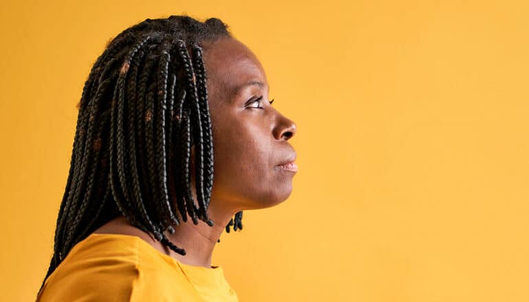 A woman wearing a yellow shirt stands in profile against a yellow background.