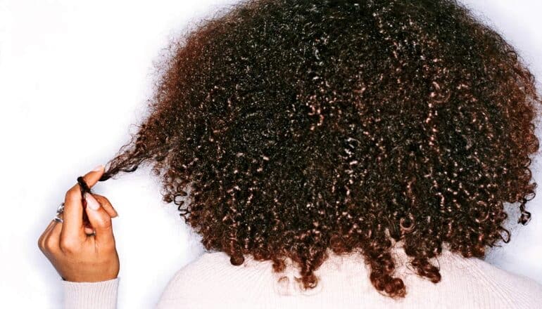 A woman with tight curly hair pulls a strand and wraps it around her finger.