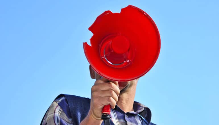 unseen person speaks into cracked red megaphone