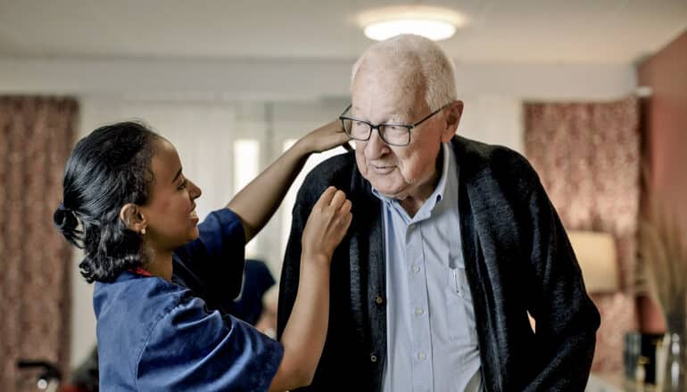 nurse adjusts sweater of elderly person indoors