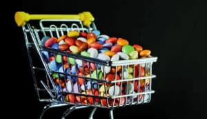 A tiny grocery cart filled with colorful candies against a black background.