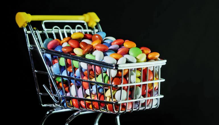 A tiny grocery cart filled with colorful candies against a black background.