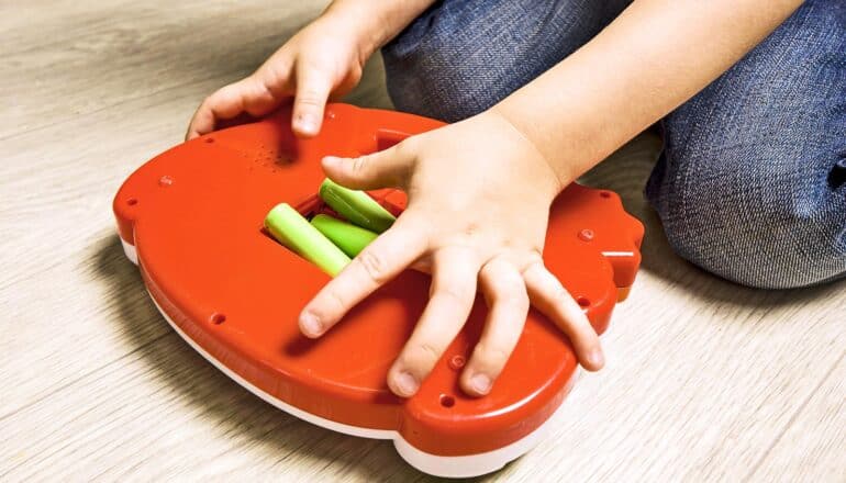 A child puts batteries into the back of a toy while sitting on the floor.