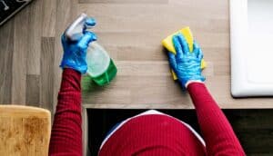 A pregnant woman cleans a kitchen counter with spray and sponge.