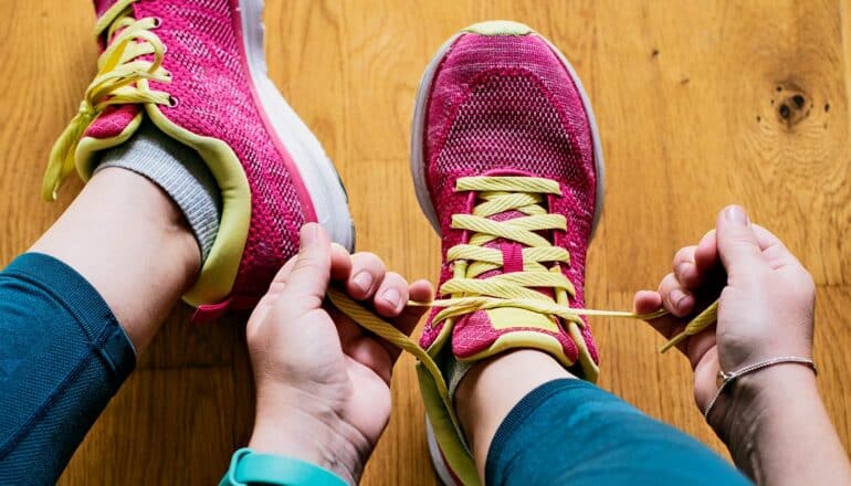 A woman ties her pink and yellow running shoes.