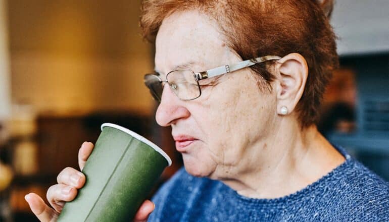 An older woman smells her cup of coffee.