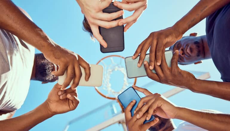 from below, four people use phones while standing in a circle on basketball court