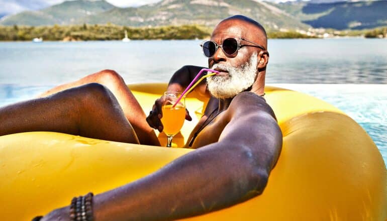 A man sits in a yellow pool tube while sipping a tropical drink.