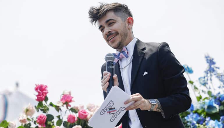 guy in suit holds mic in front of flowers