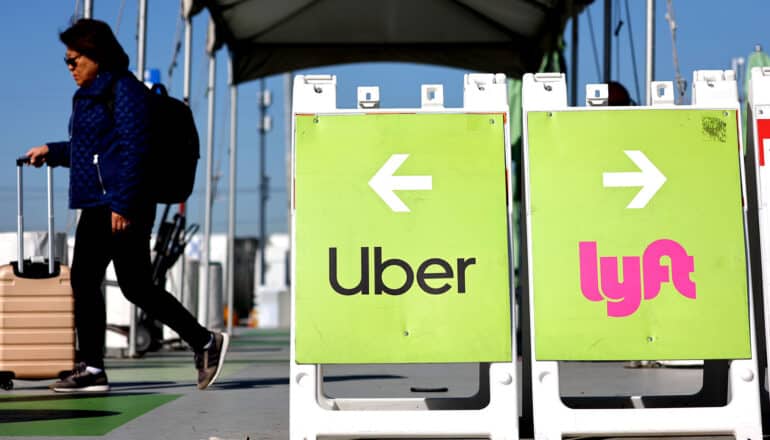 person walks past signs for Uber and Lyft