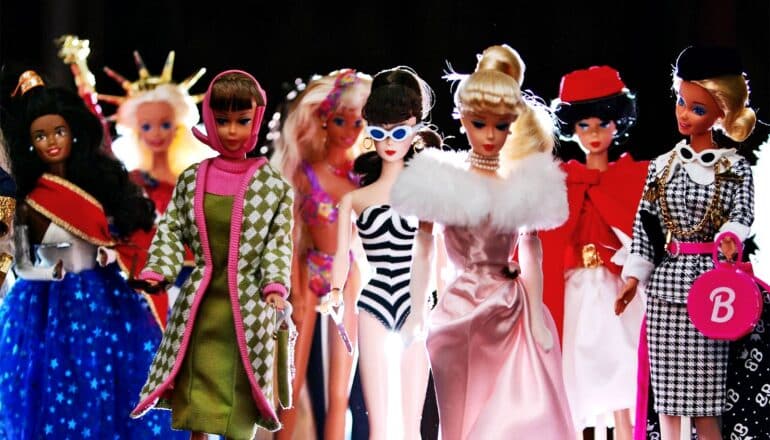 A row of Barbie dolls in different outfits against a dark background.