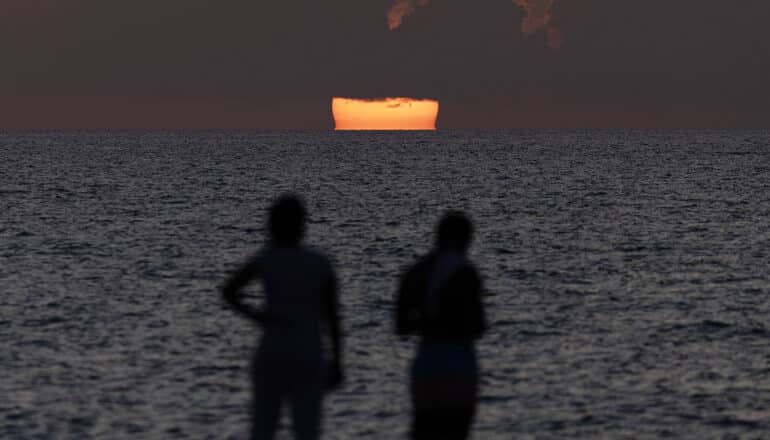 silhouetted people stand before ocean at sunrise