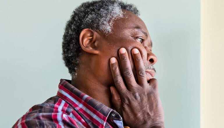 An older man touches his face and looks tired.