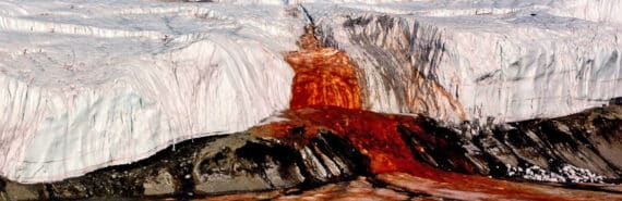 red water pours from ice over black rock