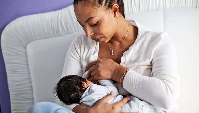 A mother breastfeeds her baby while sitting up in bed.