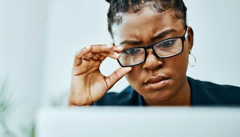 person at computer holds glasses and squints in confusion