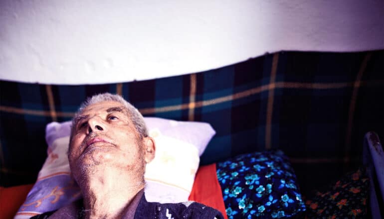 An older man lies in bed looking up at the ceiling.