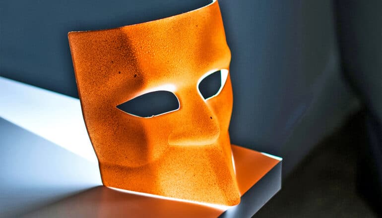 An orange face mask sits on a table in a dark room.