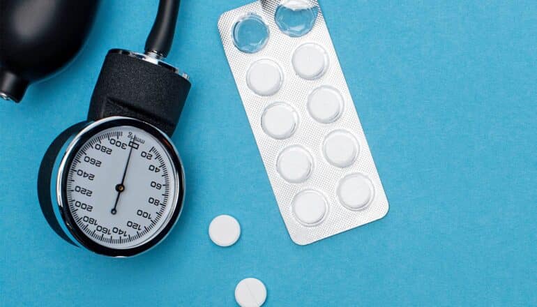 A blood pressure cuff and blister pack of white pills on a blue background.