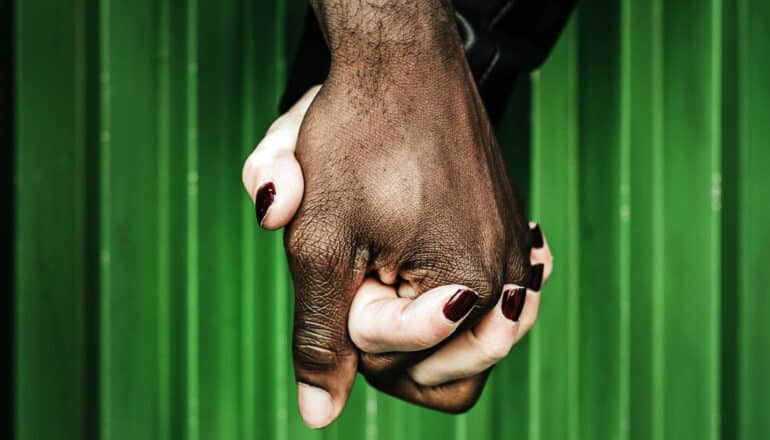 hands of interracial couple in front of green wall