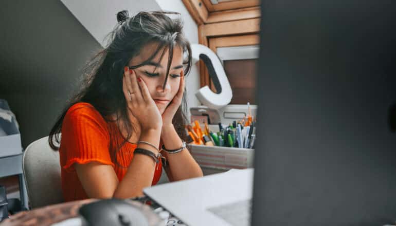 teen at laptop holds face in hands