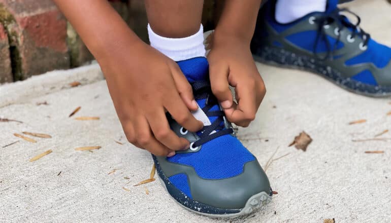 A young boy ties his shoes while sitting on his doorstep.