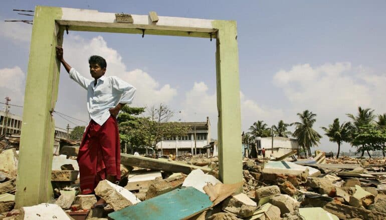 person stands in archway among rubble on coast