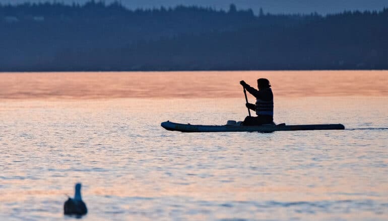 A person kayaks down a river at sunset.