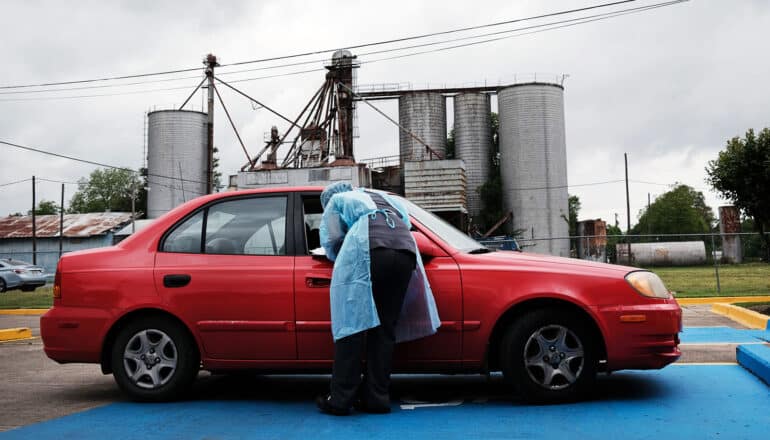 person in PPE leans into car stopped in front of grain silos