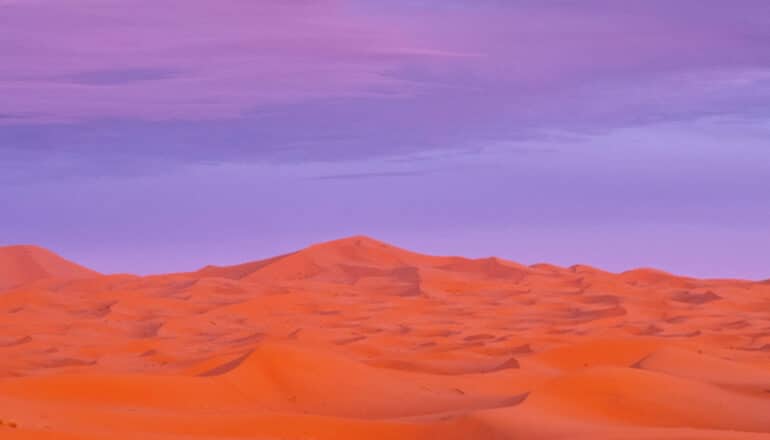 A purple sky at sunset over the reddish sand of the Sahara desert.